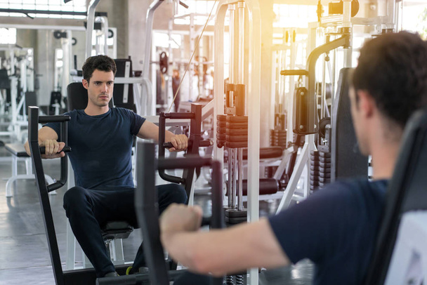 Handsome man lowering weight of fitness machine and working out  - Photo, Image