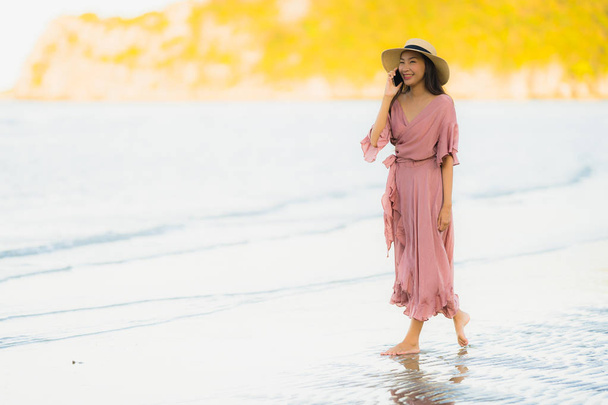 Portrait beautiful young asian woman smile happy walk with talking on mobile phone around the tropical outdoor nature beach sea for leisure vacation - Fotó, kép