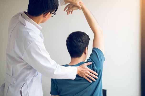 Quiropráctico estirando el brazo de un joven en el consultorio médico - Foto, Imagen