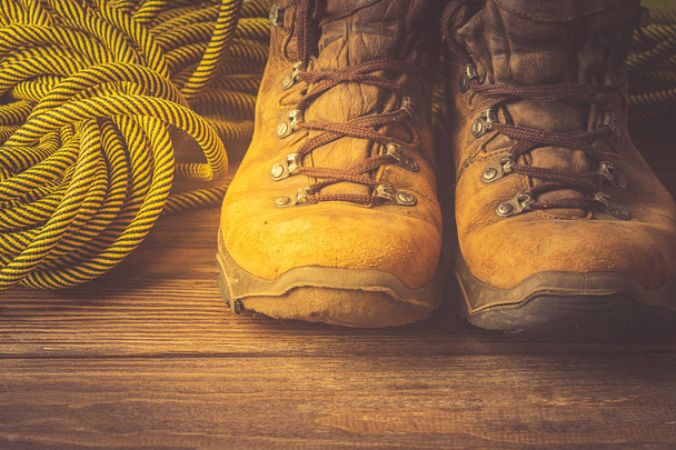 A pair of brown worn boots a sport rope on a wooden background. The concept of travel and adventure. Front view. Toning - Photo, Image