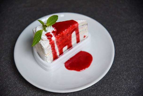 Crape cake slice with strawberry sauce on white plate on dark ba - Photo, image