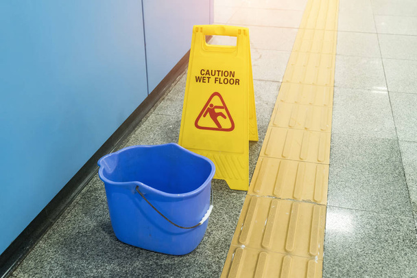 Κίτρινη Προσοχή σημάδι βρεγμένου πατώματος σε βρεγμένο πάτωμα με μπλε κουβά - Φωτογραφία, εικόνα