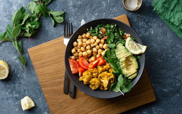 Buddha bowl. Vegetarian healthy balanced food. Aloo-gobi, chickpeas, tomato, avocado, tabule salad and spinach - Foto, imagen