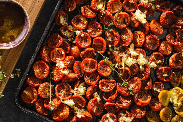 Baked juicy cherry tomatoes into a baking tray on dark background top view - Valokuva, kuva