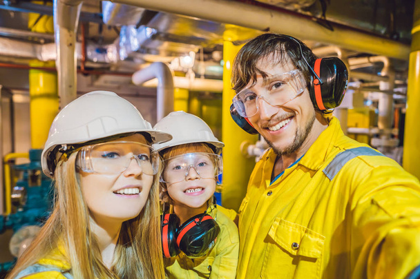 Mom, Dad and Son in a yellow work uniform, glasses, and helmet in an industrial environment, oil Platform or liquefied gas plant - Photo, Image