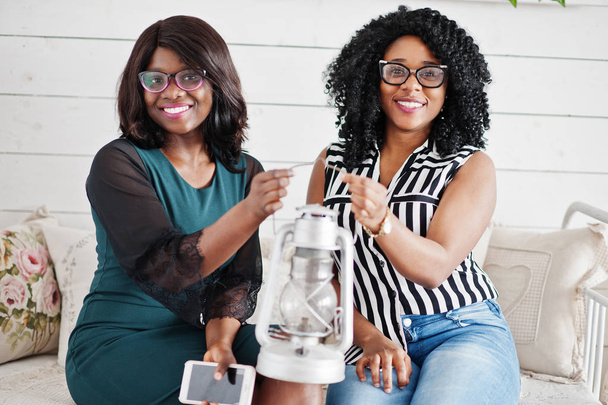 Two african woman friends wear on eyeglasses sitting at couch in - Foto, imagen