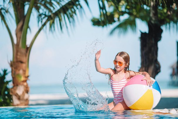 Usmívající se rozkošný dívka si hraje s nafukovací hračka míč do venkovního bazénu - Fotografie, Obrázek
