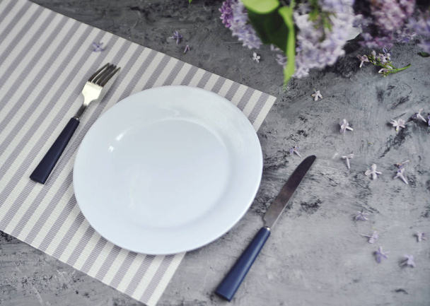 Διακοσμημένο πέτρινο τραπέζι με μαχαιροπίρουνα και λουλούδια. - Φωτογραφία, εικόνα