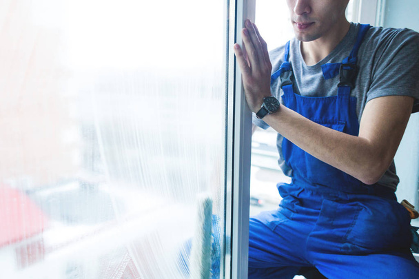 Close-up of a man in uniform and blue gloves washes a windows with window scraper. Professional home cleaning service - Zdjęcie, obraz