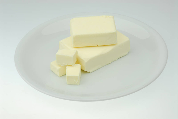 Piece of fresh organic butter on the plate isolated on a gray background in close-up - Photo, Image