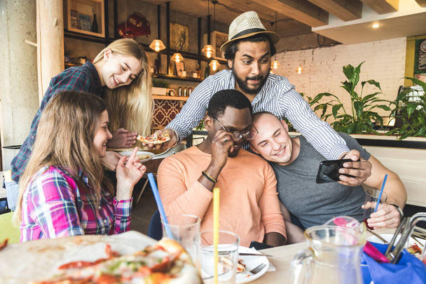 Kompania wielokulturowych młodych ludzi w kawiarni jedzących pizzę, pijących koktajle, bawiących się - Zdjęcie, obraz