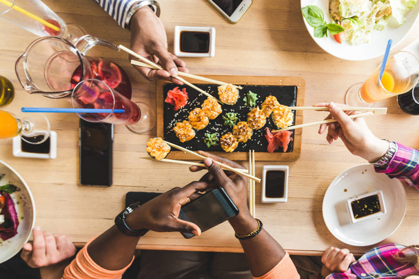 Top view. A company of multicultural company young people in a cafe eating sushi rolls, drinking drinks having fun - 写真・画像