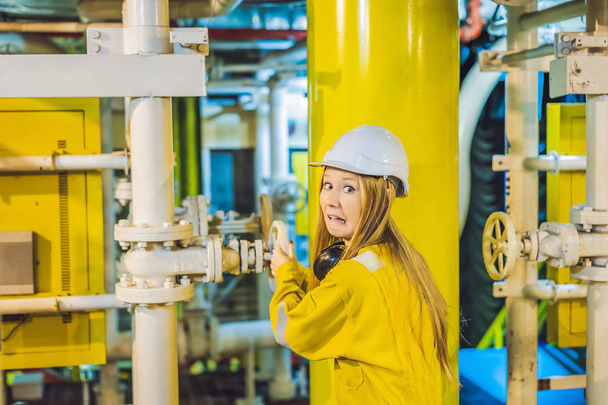 Fiatal nő sárga munkaruha, szemüveg és sisak ipari környezetben, olaj platform vagy cseppfolyósított gáz üzem - Fotó, kép