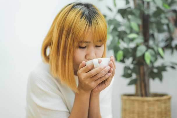 Atraente bela mulher asiática desfrutando de café quente na cozinha em sua casa. Mulher asiática vestindo camisola confortável segurando uma xícara de café. estilo de vida mulher asiática em casa conceito
. - Foto, Imagem