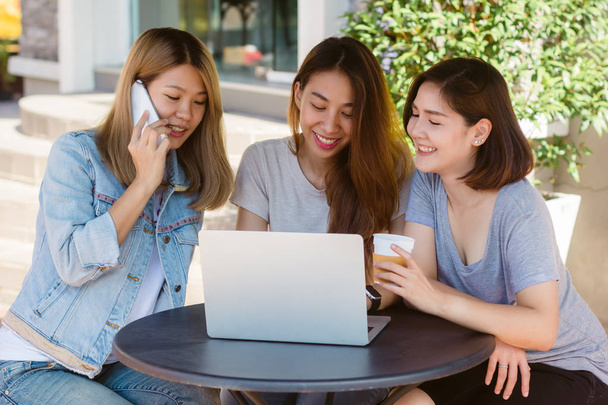 Молодые азиатки, работающие на ноутбуке, смотрят на смартфон и пьют кофе, сидя в кафе. Общение женщин в стиле жизни и работа в концепции кафе
. - Фото, изображение