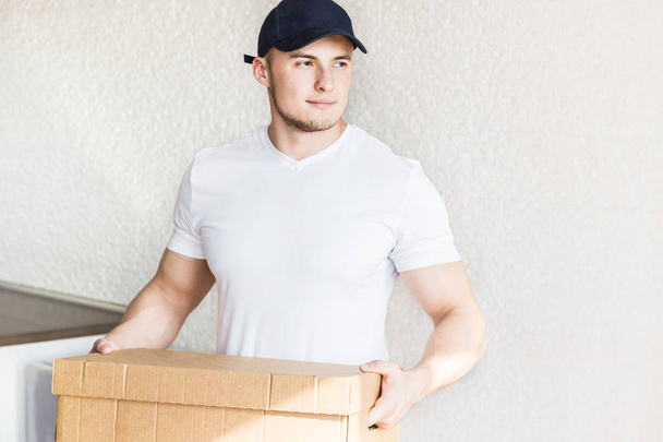 Delivery strong, muscular man loading cardboard boxes for moving to an apartment. professional worker of transportation, male loaders in overalls. free space for text, isolated - Фото, зображення