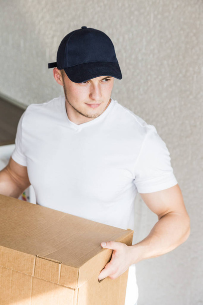 Delivery strong, muscular man loading cardboard boxes for moving to an apartment. professional worker of transportation, male loaders in overalls. free space for text, isolated - 写真・画像