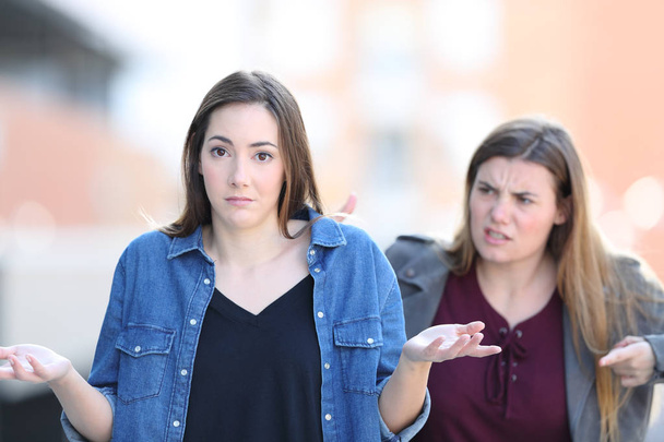 Woman scolding her confused friend who looks at you - Фото, изображение