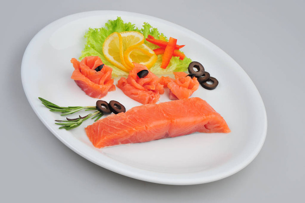 Fresh salmon decorative roses fillets, with lemon, olives on the plate. Isolated on a gray background - Photo, Image