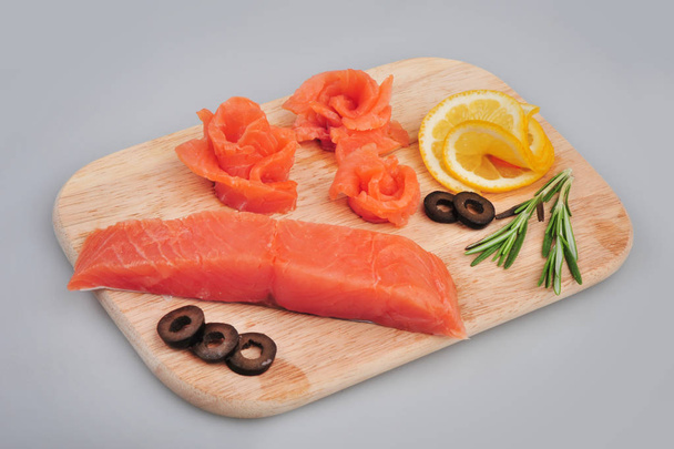Fresh salmon decorative roses fillets, with lemon, olives on the board. Isolated on a gray background - Photo, Image