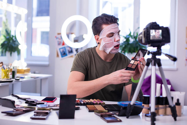 Curious interested man in face mask opening eyeshadow palette - 写真・画像