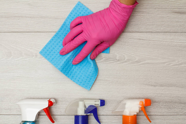 Hand in Gummihandschuh hält Serviette mit Waschmittelflaschen auf Holzgrund. - Foto, Bild