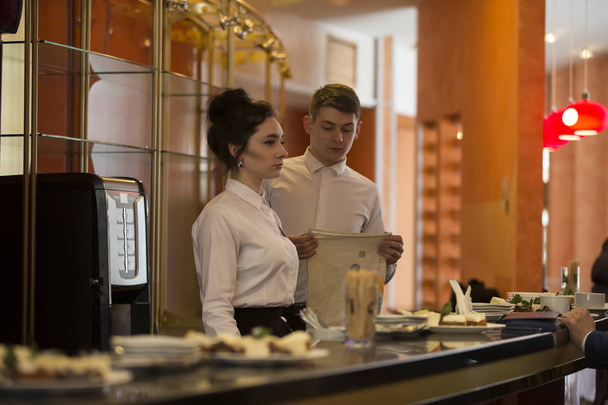 Wit-Rusland, Vitebsk, 27 februari 2019. City restaurant. Food Festival ober met een lade. Twee barmannen een man en een vrouw aan de balie. Obers werken - Foto, afbeelding