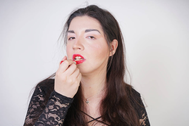 Asiatique femme heureuse peint ses lèvres avec du rouge à lèvres sur fond de studio blanc. Mauvaise tentative de bien se réconcilier. Adulte fille apprend à peindre son visage
. - Photo, image