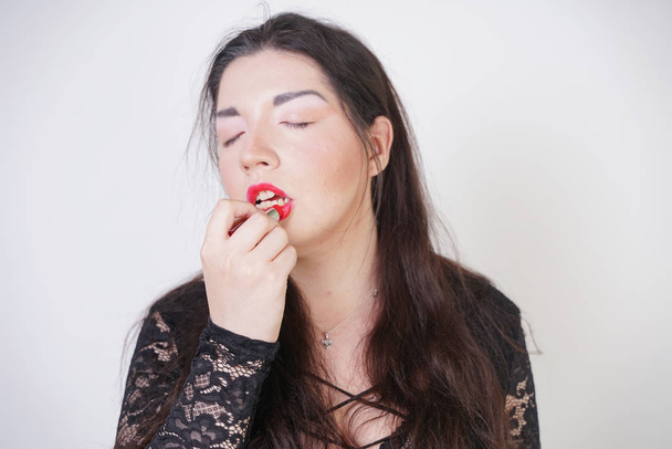Aziatische gelukkige vrouw schildert haar lippen met Lipstick op witte studio achtergrond. Verkeerde poging om goed zelf make-up. Volwassen meisje is leren om haar gezicht te schilderen. - Foto, afbeelding