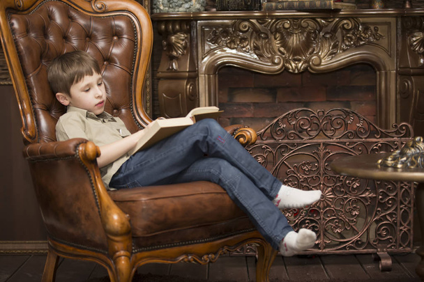Дитина в кріслі читає книгу. Маленький хлопчик з книгою
 - Фото, зображення