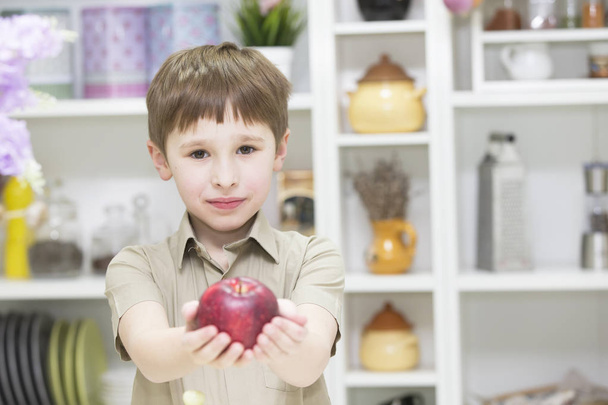 El niño en la cocina sostiene una manzana roja. El niño muestra fruta.
 - Foto, imagen