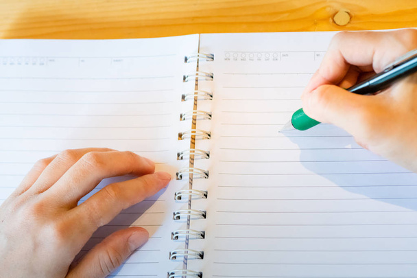 θηλυκό χέρι με μολύβι γράφοντας στο σημειωματάριο στην καφετέρια. - Φωτογραφία, εικόνα