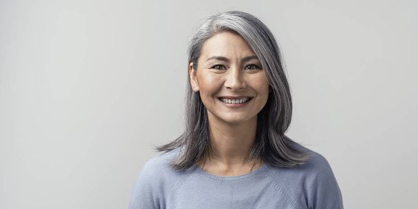 Beautiful asian with grey hair smiling standing near the wall - Фото, зображення