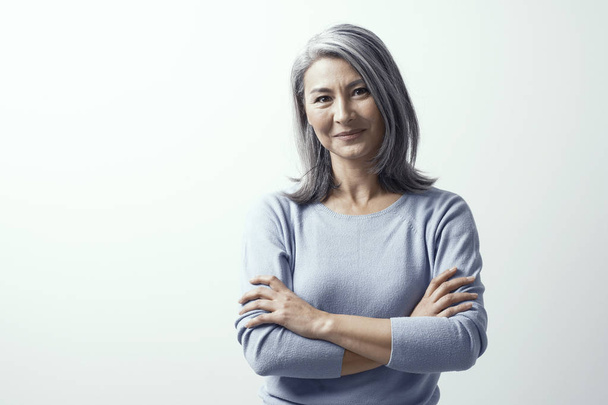 Beautiful woman with gray hair standing near the wall hands crossed - Photo, image