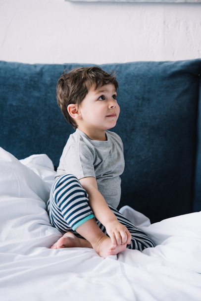 cute kid sitting on bed with white bedding at home  - Photo, Image