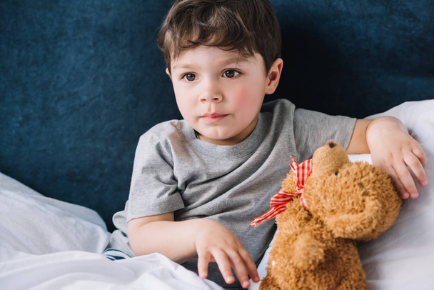 cute child sitting near teddy bear in bedroom at home  - Fotografie, Obrázek