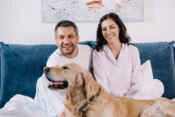 selective focus of happy man and woman near cute golden retriever in bedroom  - Foto, Imagem
