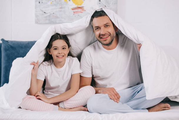 happy father sitting with cute daughter and holding blanket on bed  - Φωτογραφία, εικόνα