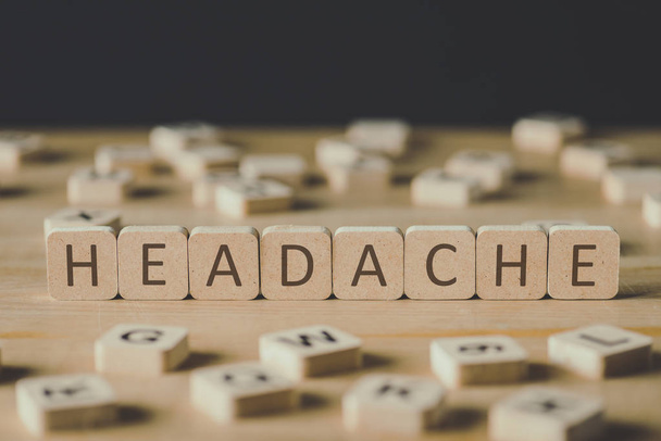 selective focus of headache lettering on cubes surrounded by blocks with letters on wooden surface isolated on black - Photo, image