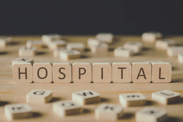 黒で隔離された木製の表面に文字を持つブロックに囲まれた単語病院を持つキューブの選択的な焦点 - 写真・画像