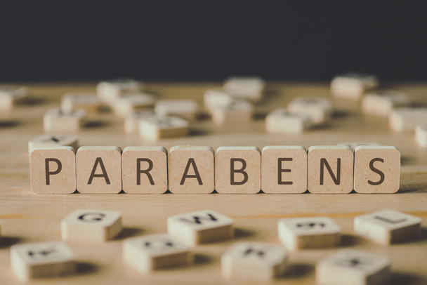 selective focus of word parabens made of cubes surrounded by blocks with letters on wooden surface isolated on black - Фото, изображение