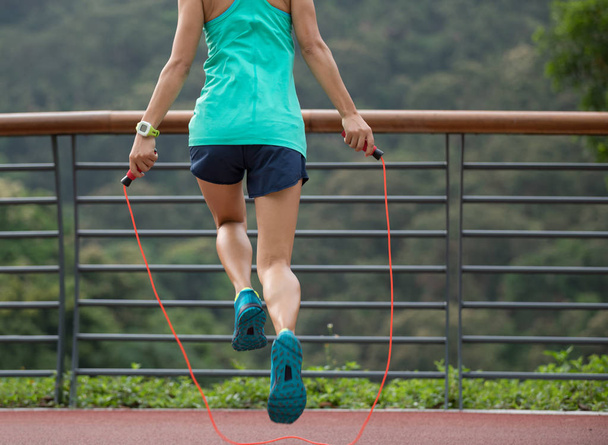 Woman athlete training with jumping rope on spring forest trail. wellness concept. - 写真・画像