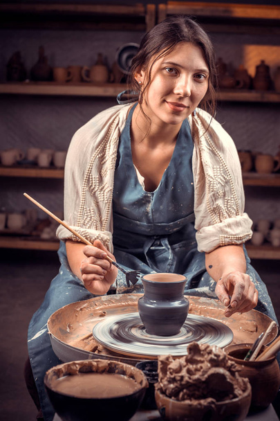 手で生の粘土で陶器の車輪に取り組むスタイリッシュな若くて陽気な女性。セラミック料理の作り方. - 写真・画像