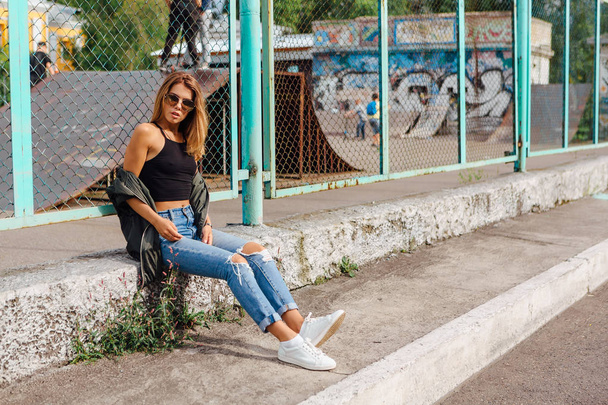 Fashion portrait of trendy young woman wearing sunglasses, and bomber jacket sitting next to rabitz in the city - Fotografie, Obrázek