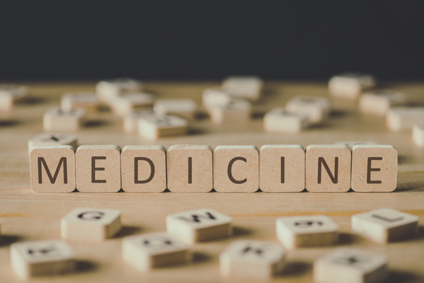 selective focus of medicine lettering on cubes surrounded by blocks with letters on wooden surface isolated on black - 写真・画像