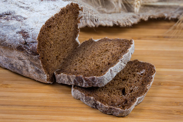Deels gesneden bruin brood op houten oppervlak close-up - Foto, afbeelding