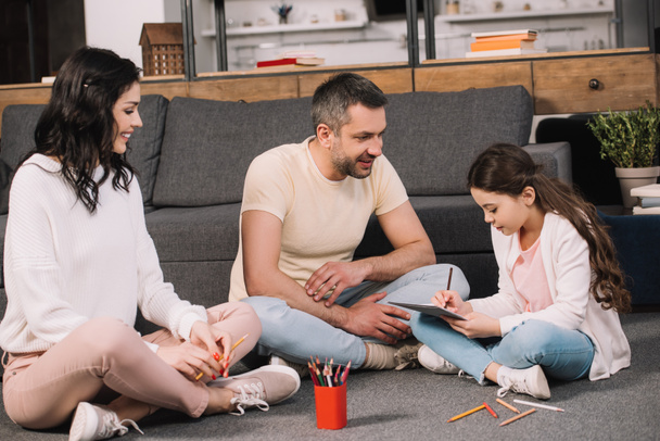 happy parents sitting on floor near cute daughter drawing on paper  - Photo, Image