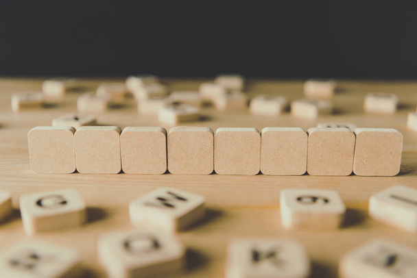 selective focus of eight blank cubes surrounded by blocks with letters on wooden surface isolated on black - Foto, Imagem