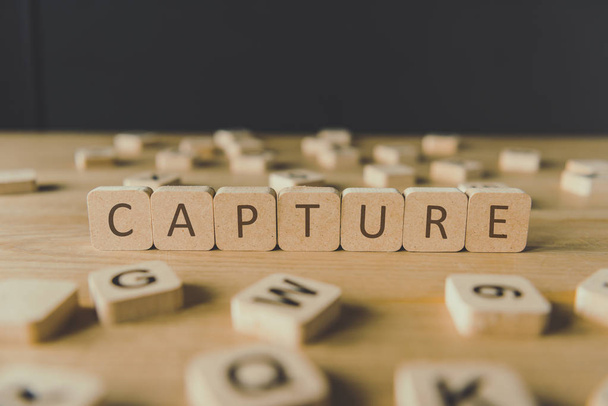 selective focus of word capture made of cubes surrounded by blocks with letters on wooden surface isolated on black - Foto, Imagen