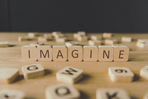 selective focus of word imagine made of cubes surrounded by blocks with letters on wooden surface isolated on black - Photo, Image